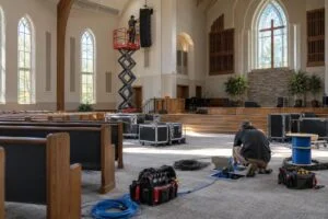 Technicians installing a line-array speaker and cabling in an empty church sanctuary (illustration)